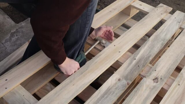 A young man disassembles a pallet. A wooden pallet, garden furniture. A man rips off the boards to make a table. Cheap DIY master eco-friendly wasteless with their own hands top