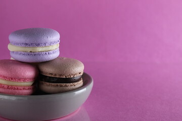 Macaroons three multicolored on a gray saucer plate stands on a pink background with a place for text and copyspace