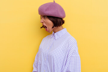 Young mixed race woman wearing a beret isolated on yellow background shouting towards a copy space