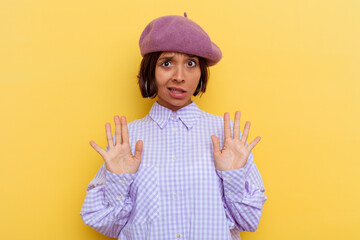 Young mixed race woman wearing a beret isolated on yellow background rejecting someone showing a gesture of disgust.