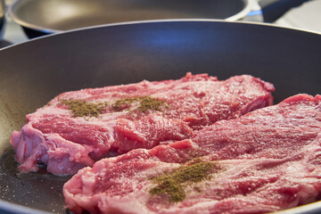 Red meat steaks with black pepper in a frying pan.