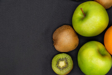 photo of fruit on a dark background. Orange, apple, kiwi