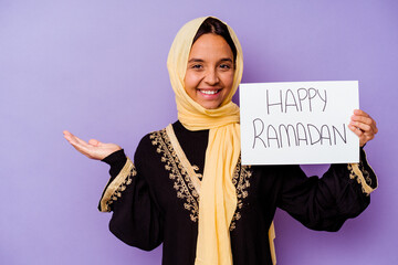 Young Moroccan woman holding a happy ramadan placard isolated on purple background showing a copy...
