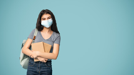 Teen Indian girl wearing medical mask, posing with backpack and books, following quarantine...