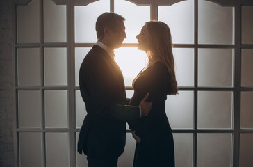 Silhouette of pregnant woman and her husband near the window.