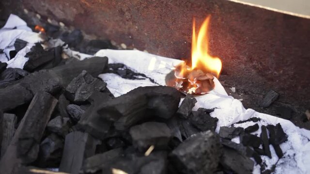 A young man lights a fire with paper matches and coals. Metal grill. Rest in nature, patio Bonfire for cooking
