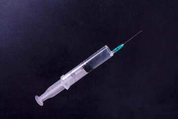 A syringe with a vaccine floating in the air. Against a dark background. Close-up.