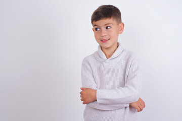 Dreamy rest relaxed Caucasian kid boy wearing knitted sweater against white wall  crossing arms, looks good copyspace