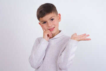 Funny Caucasian kid boy wearing knitted sweater against white wall hold open palm new product great...