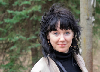 Fototapeta premium portrait of a charming middle-aged 45 years old woman with dark long hair with beautiful eyes who stands in the park and smiles