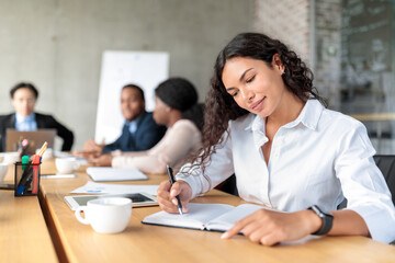 Businesswoman Writing In Notebook Sitting At Conference Meeting In Office