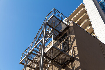 Modern fire escape staircase on the wall of a multi-storey building against a blue sky