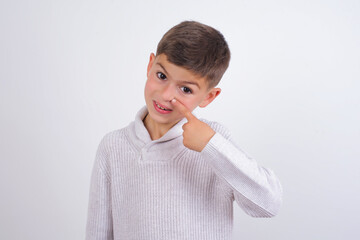 Caucasian kid boy wearing knitted sweater against white wall pointing unhappy to pimple on...