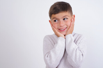 Inspired Caucasian kid boy wearing knitted sweater against white wall looking at copyspace having thoughts about future events