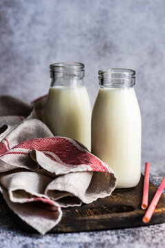 Two Bottles Of Milk And Drinking Straws On A Wooden Chopping Board With A Tea Towel