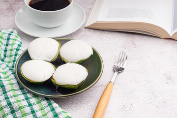 Top view of Thai pudding with coconut topping on a plate with a book, a white coffee cup, and a cloth placed on a gray stone background. Space for text. Concept of relaxation