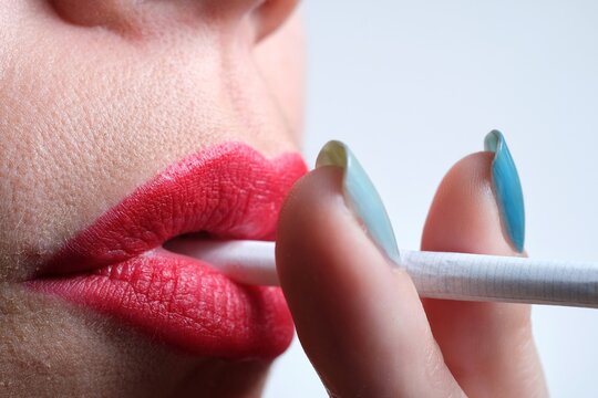 Close up of a woman with sensual red lips and green fingernails smoking a cigarette