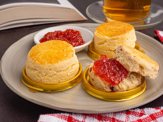Side view of scones traditional English delicious fresh bake homemade with strawberry jam placed on a plate with a book, and a teacup. Close-up photo. Dessert, beverage, and relaxation concept