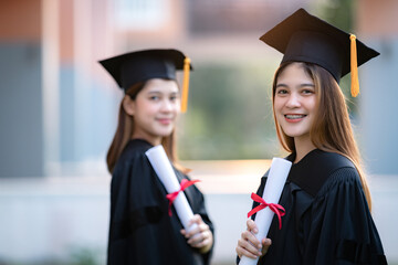 Young happy Asian woman university graduates in graduation gown and mortarboard hold a degree certificate celebrate education achievement in the university campus.  Education stock photo