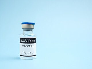COVID-19 vaccine in a glass bottle placed on a light blue background. Vaccine for immunization, and treatment from coronavirus infection. Side view. Close-up photo. Concept of medical and healthcare