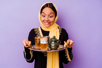 Young Moroccan woman holding a glass of tea isolated on purple background