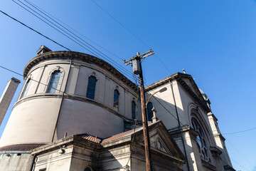 Old light stone church against a bright blue sky, power lines and pole, horizontal aspect