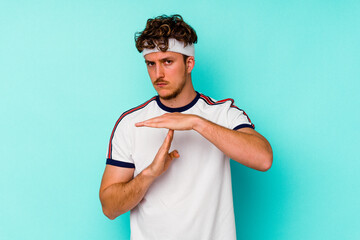 Young sport caucasian man isolated on blue background showing a timeout gesture.