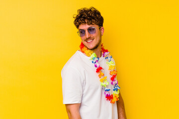 Young caucasian man wearing a Hawaiian party stuff isolated on yellow background looks aside...