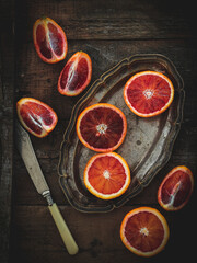 Obraz na płótnie Canvas Sliced blood oranges on a vintage saucer and knife, dark mood, flat lay style