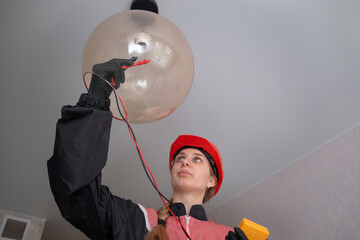 Electrician technician measures the voltage in the lamp socket of a residential electrical system and changes the light bulb. female electrician using a multimeter	