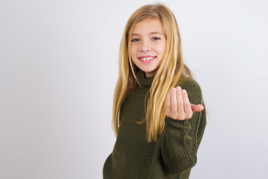 Caucasian kid girl wearing green knitted sweater against white wall inviting to come with hand. Happy that you came