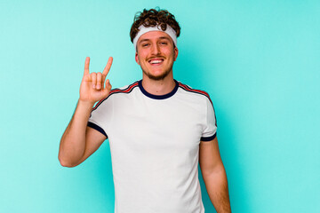 Young sport caucasian man isolated on blue background showing a horns gesture as a revolution concept.