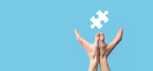 Male hand holding puzzle icon on blue background. pieces representing the merging of two companies or joint venture, partnership, Mergers and acquisition concept.
