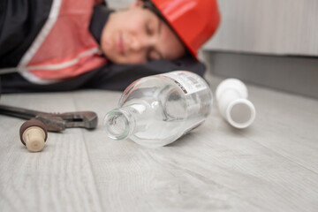 a drunken plumber in uniform and hard hat sleeps on the floor, with tools and an empty bottle scattered nearby. Alcohol addiction at work	