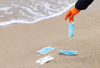 Volunteer picking face masks from ocean beach, sea plastic pollution concept