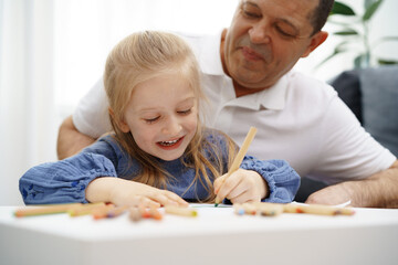Fototapeta premium Grandfather and granddaughter drawing together in living room