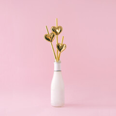 Celebration bottle with gold tubes with hearts. Pastel pink background.