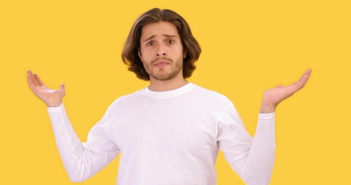 Studio portrait of young upset guy outstretching hands in ignorance, feeling confused, yellow background