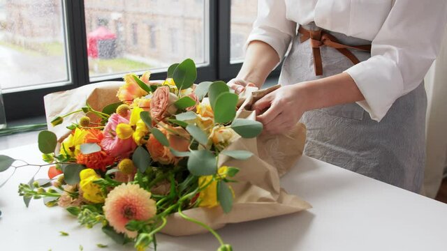people, gardening and floral design concept - happy woman wrapping flowers to craft paper at home