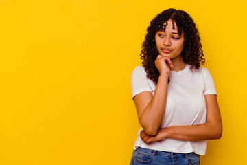 Young mixed race woman isolated on yellow background looking sideways with doubtful and skeptical expression.