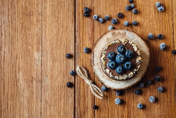 Delicious tartlet with fresh blueberries and chocolate, on wooden background. Trendy dessert. Place for text. copied space