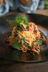 spaghetti pasta with tomato sauce,bacon and basil black disk plate on wood table and medium shot.