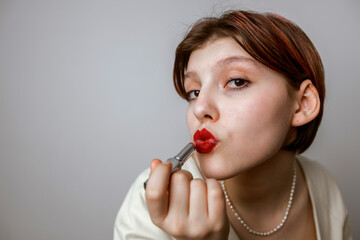 The girl paints her lips with red lipstick. Portrait on a light background close-up