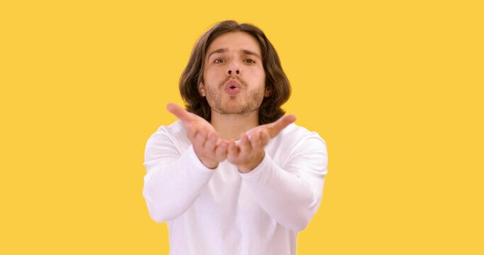 Lovelace. Young man sending blow kiss to camera with both hands, smiling over yellow studio background, slow motion