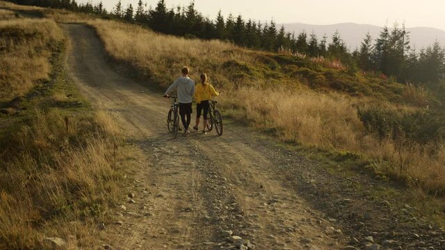 Man and woman with bikes going on road. Cyclists taking break after exercising