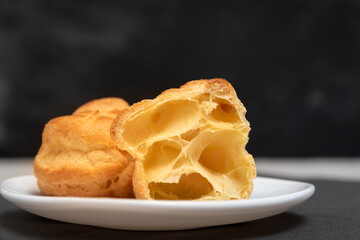 Profiteroles on white saucer on black background, close up. Preparation for eclairs.