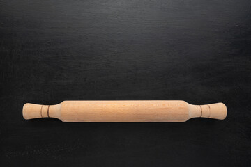 Wooden rolling pin on black background, top view. Copy space, kitchen concept