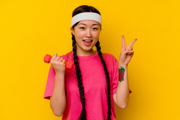 Young sport chinese woman isolated on yellow background joyful and carefree showing a peace symbol with fingers.