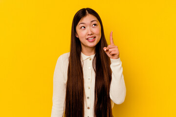 Young chinese woman isolated on yellow background indicates with both fore fingers up showing a...