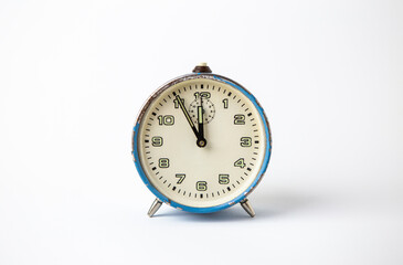 Old analog blue clock on a white background. The clock shows the time from five minutes to twelve o'clock.